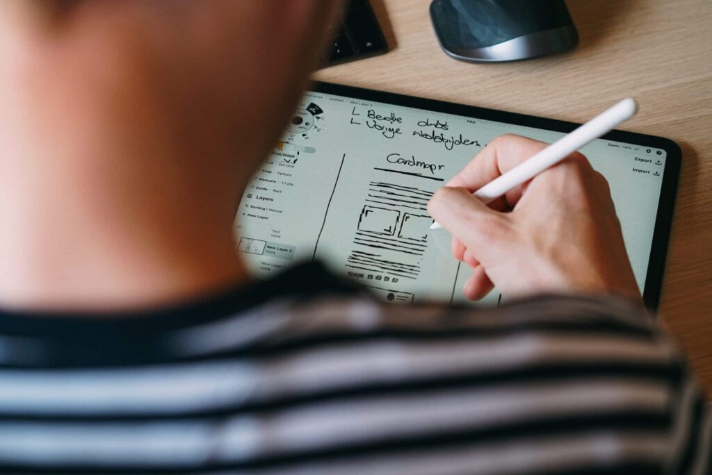 Un Webdesigner crée un wireframe sur une tablette en utilisant un stylet pour dessiner les différentes zones de contenu, les boutons de navigation et les formulaires.